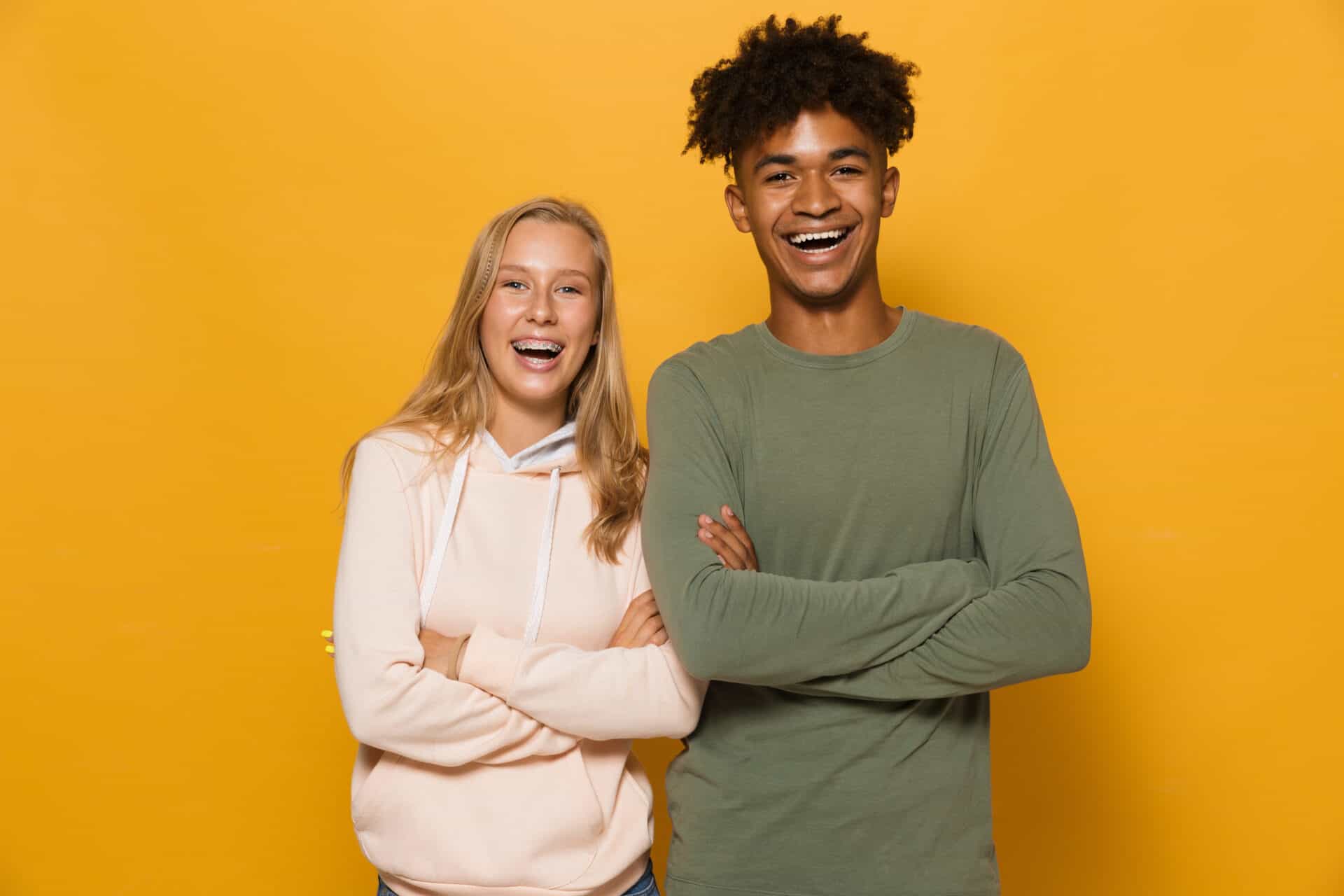 Photo of happy students man and woman 16-18 with dental braces laughing at camera, isolated over yellow background